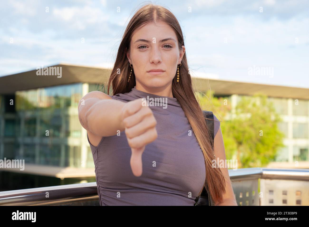 portrait Young angry caucasian woman pointing thumb down looking thoughtful outdoors.  Stock Photo