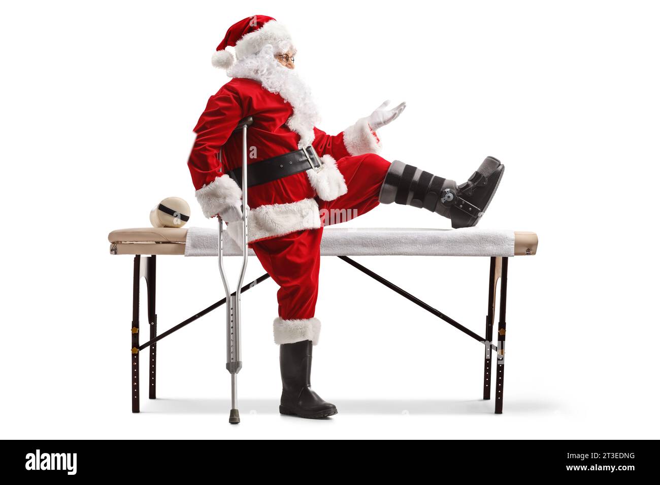 Santa claus with a foot brace and crutch sitting on a medical bed and gesturing with hand isolated on white background Stock Photo