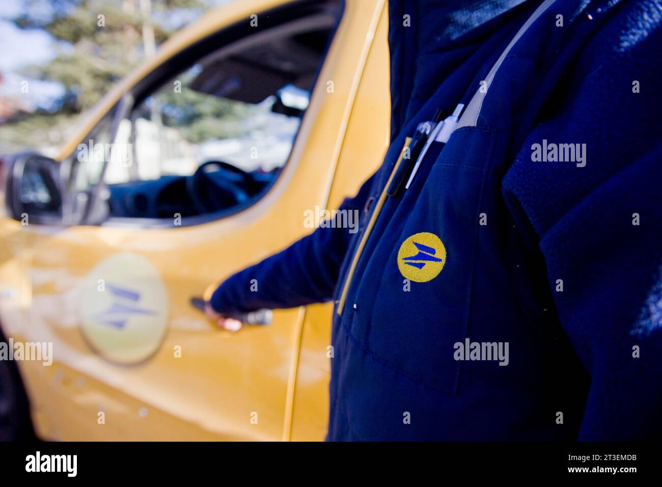 Close-up shot of the logo of La Poste, mail service of France, on the jacket of a mailman in front of his vehicle Stock Photo