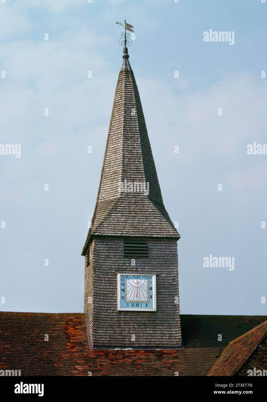 Board sundial on the S face of the bell turret with a broach spire on the tiled roof of St Michael and All Angels' Church, Thursley, Surrey, England. Stock Photo