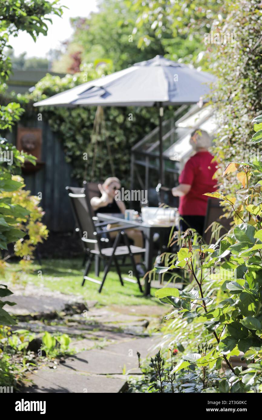 Concept, showing selective focus of two out of focus people in a garden setting, with the foreground of  shrubs and bushes in focus, as if overlooked Stock Photo