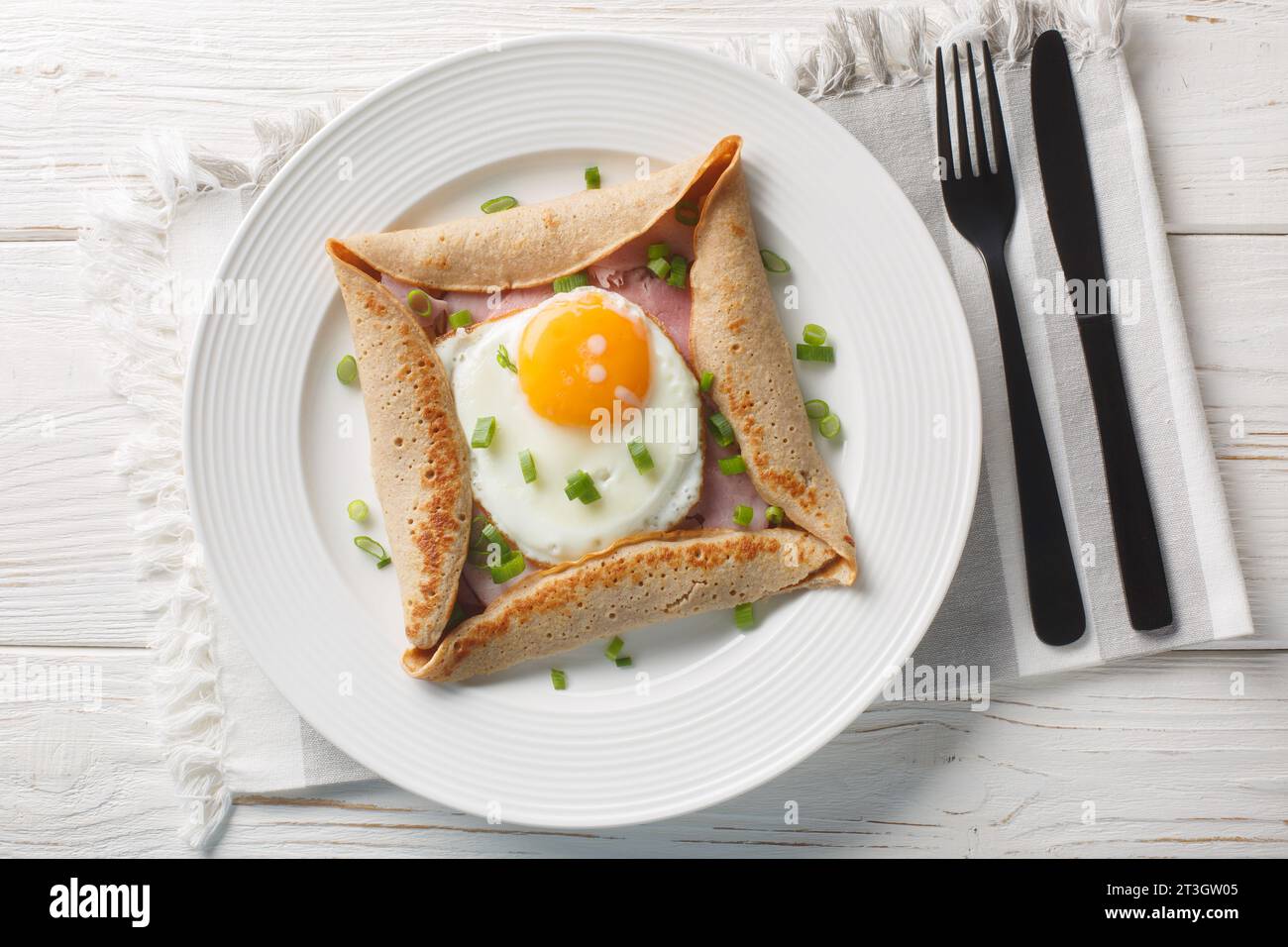 Galette complete Breton buckwheat pancake with egg cheese and ham closeup on the plate on the table. Horizontal top view from above Stock Photo