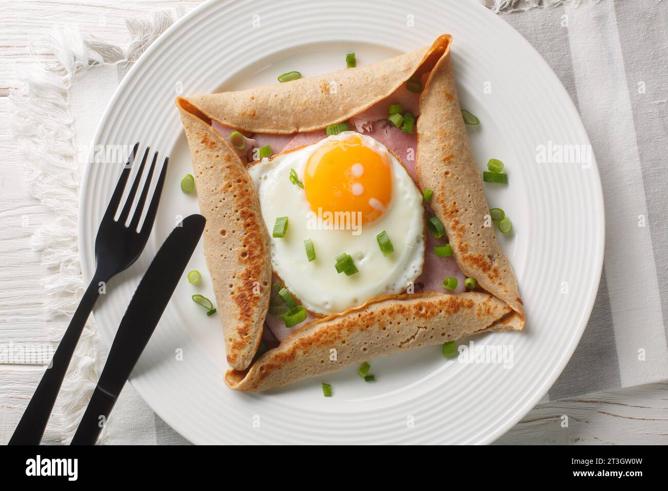 Breton galette, galette sarrasin, buckwheat crepe, with fried egg, cheese, ham closeup on the plate on the table. Horizontal top view from above Stock Photo