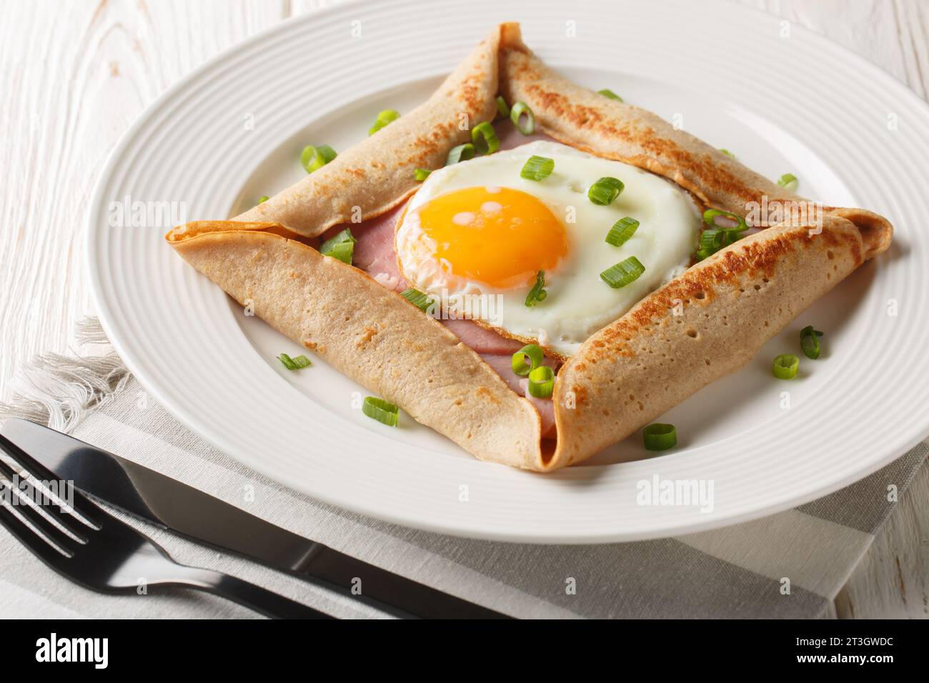 Breton galette, galette sarrasin, buckwheat crepe, with fried egg, cheese, ham closeup on the plate on the table. Horizontal Stock Photo