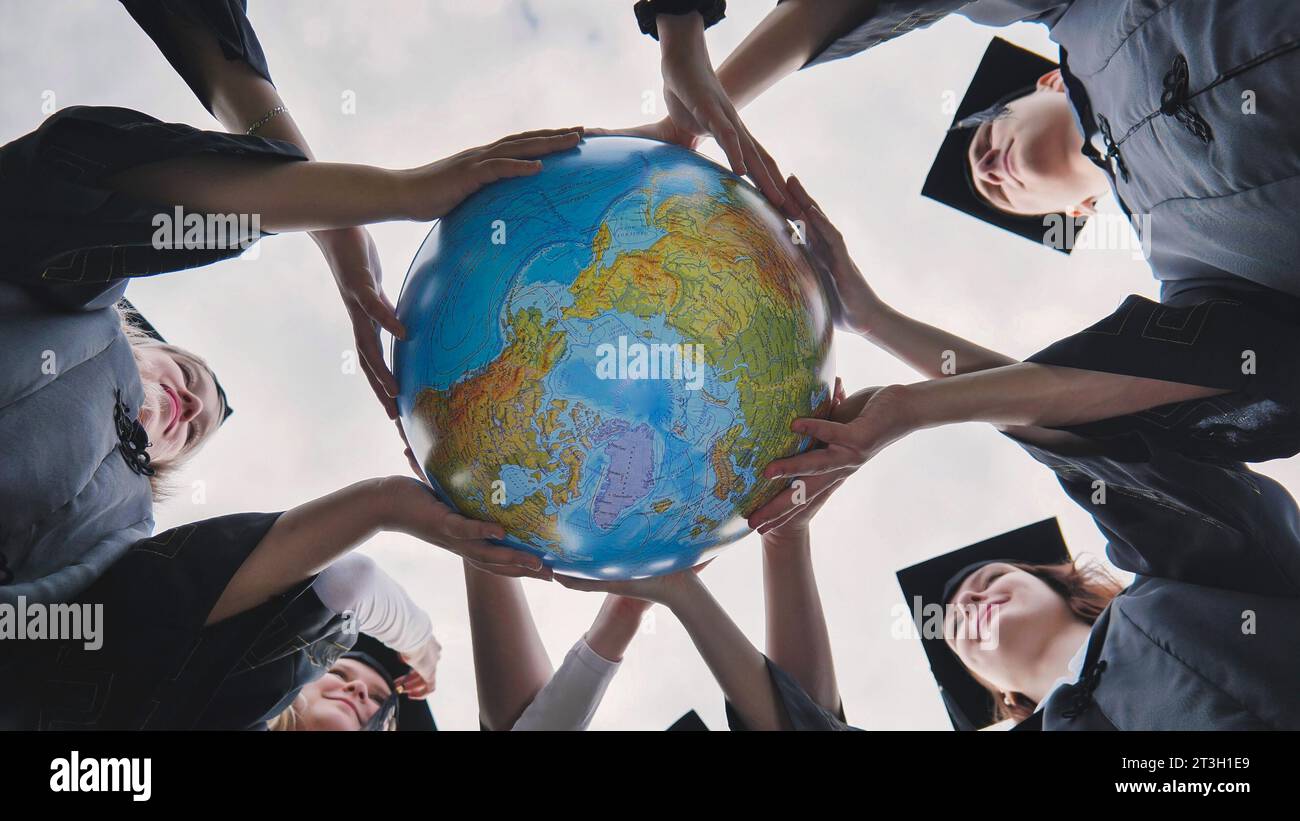 Graduating students twirl and toss a geographical globe of the world. Stock Photo