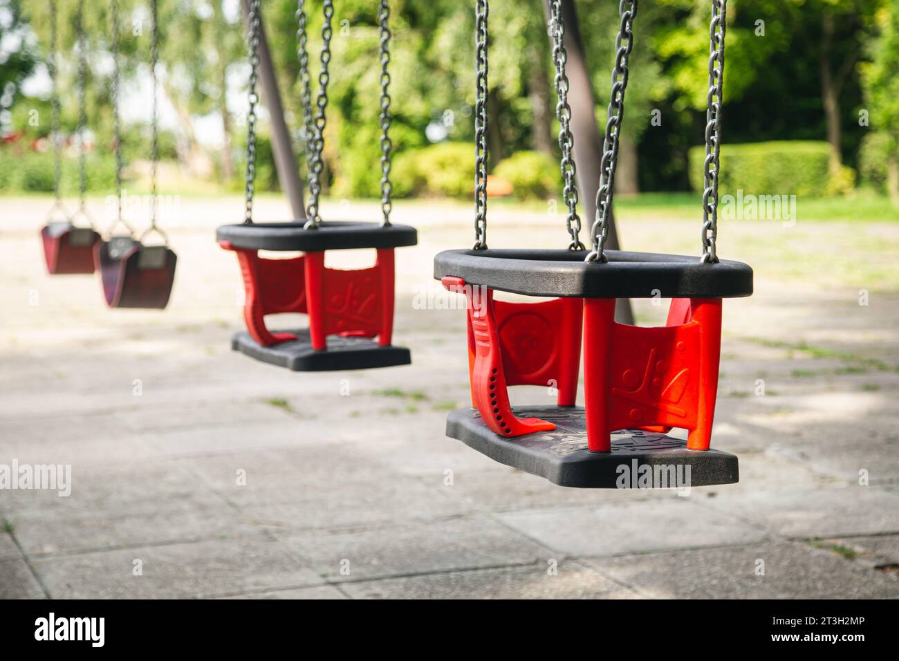 Red plastic swings hanging from chains in a children’s park Stock Photo