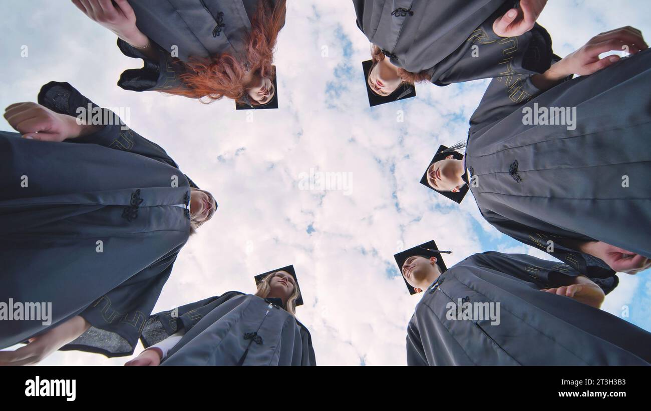 Graduates in black robes stand in a circle. Stock Photo