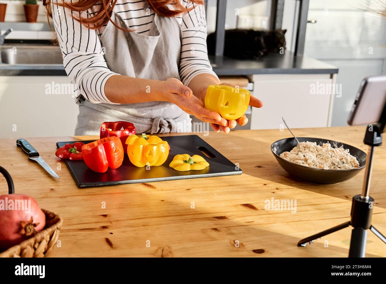 Woman food blogger preparing stuffed colorful bell peppers with ricotta cheese for Halloween party. Peppers carved like Jack-o-lantern scary face. Hal Stock Photo