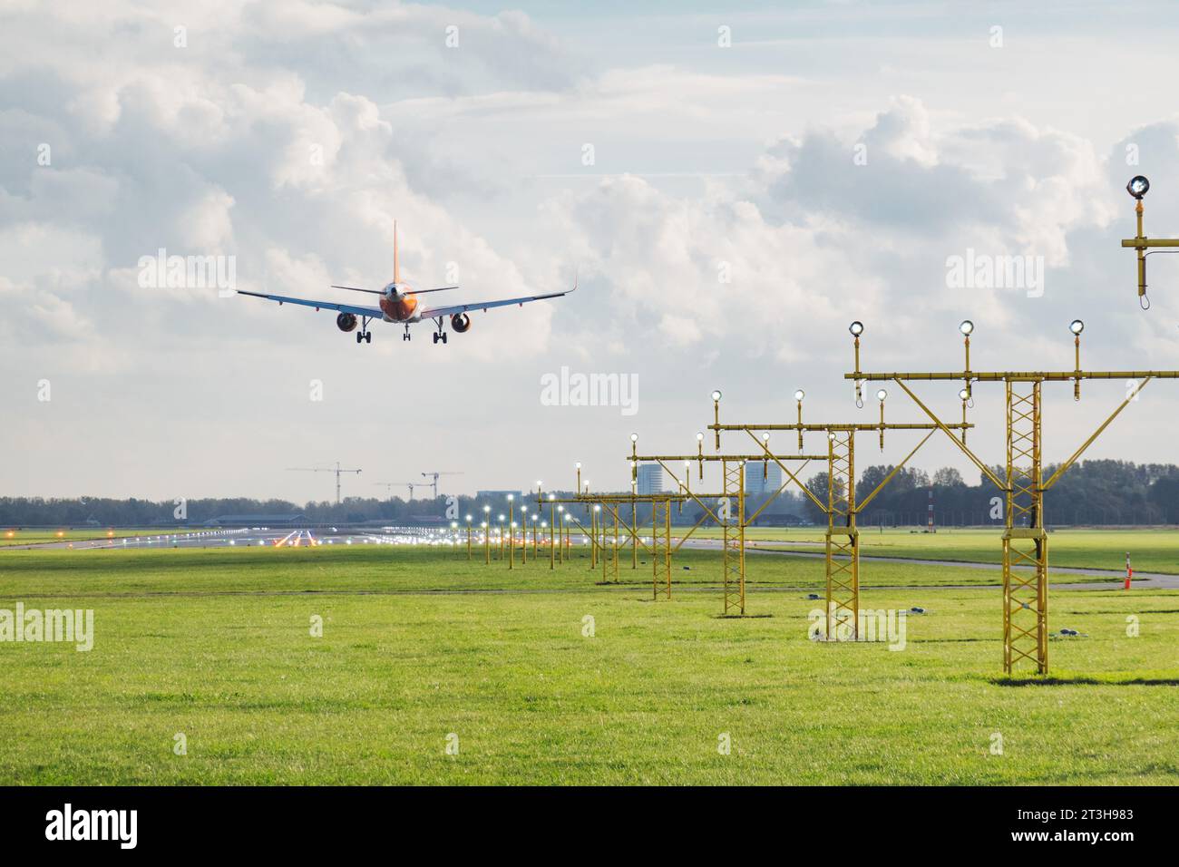 an Airbus A320 jet flies over approach lights landing on Amsterdam Schiphol airport's Polderbaan runway on a sunny autumn afternoon Stock Photo