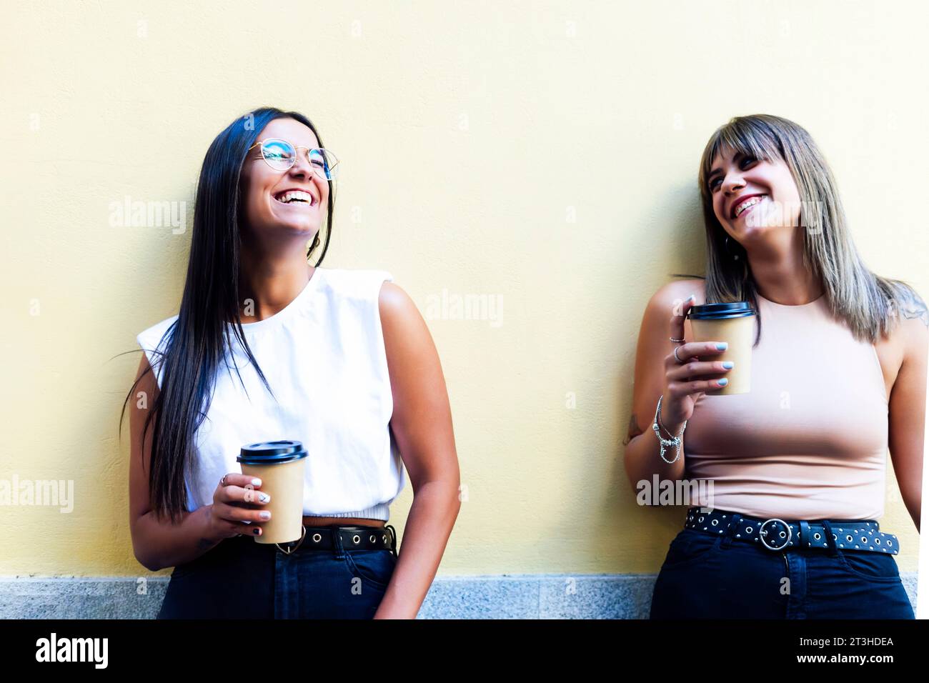 Two happy friends talking outside on the street with two coffees in hand. Stock Photo