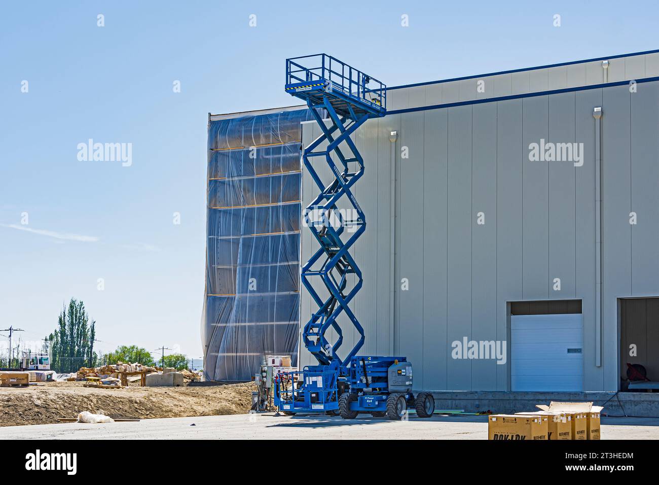 A large rental scissor-lift is used to transport personnel and materials to the roof at a construction site. Stock Photo