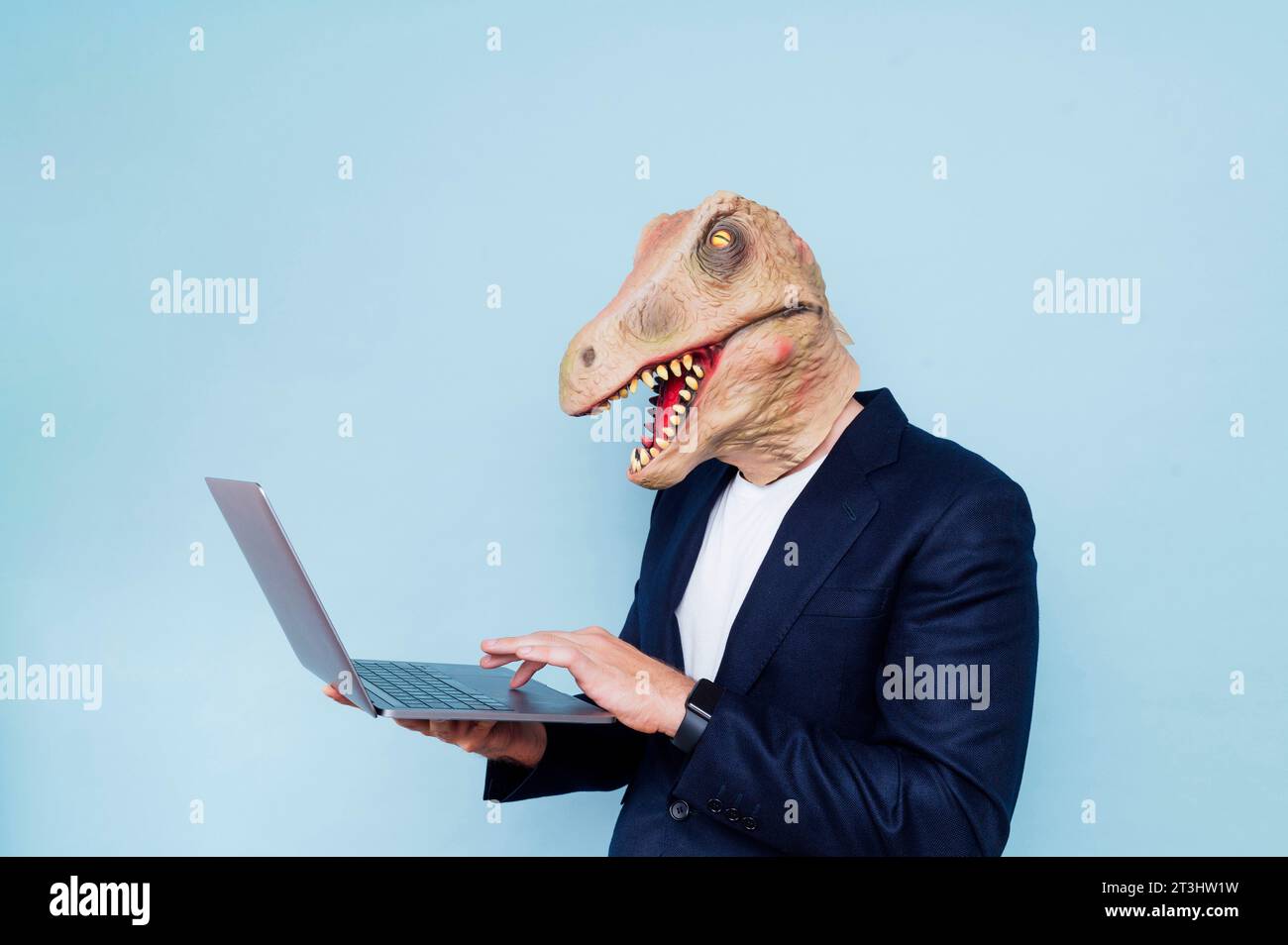 man in dinosaur mask using laptop.Blue background Stock Photo