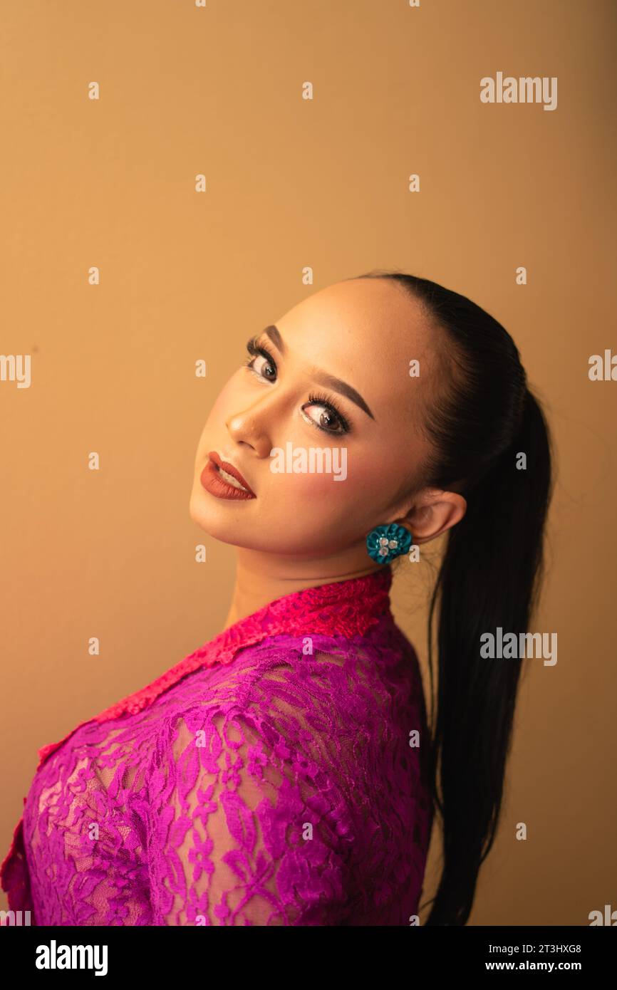 Javanese woman with black hair wearing makeup and a pink dress called kebaya in Indonesia festival event Stock Photo