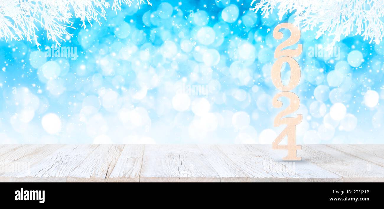 Happy New Year 2024 Wooden Numbers on white vintage planked wood table in perspective on bright blue bokeh winter background with white snowy branches Stock Photo