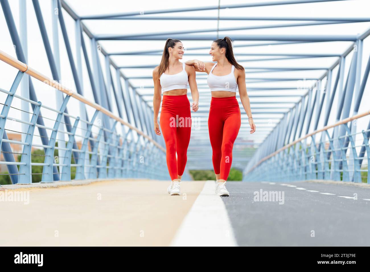 Two female friends jogging across a city bridge. They relax after