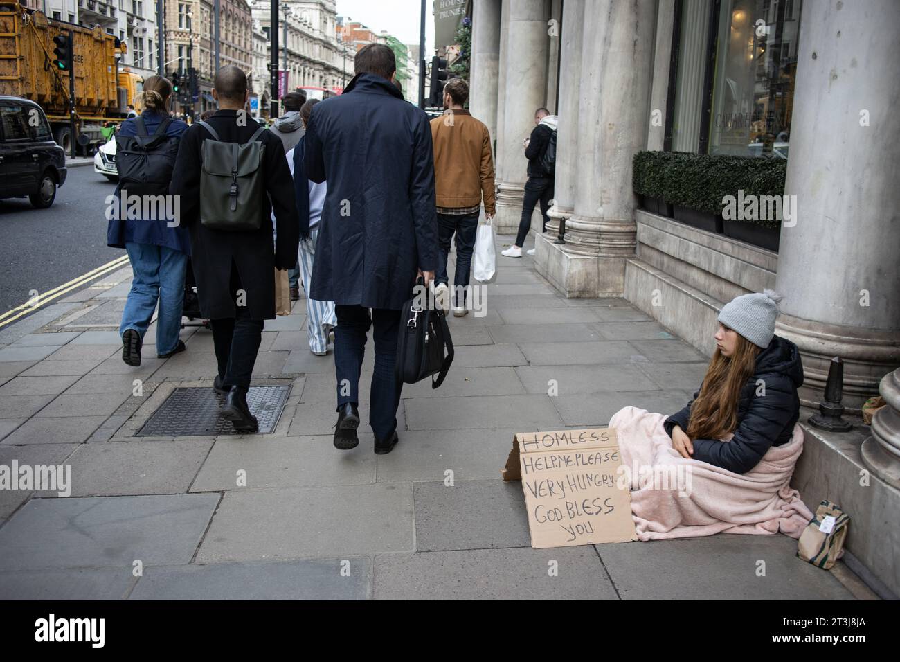 A homeless woman sits outside The Wolesley as businessmen walk past, Piccadilly, London, England, UK Stock Photo