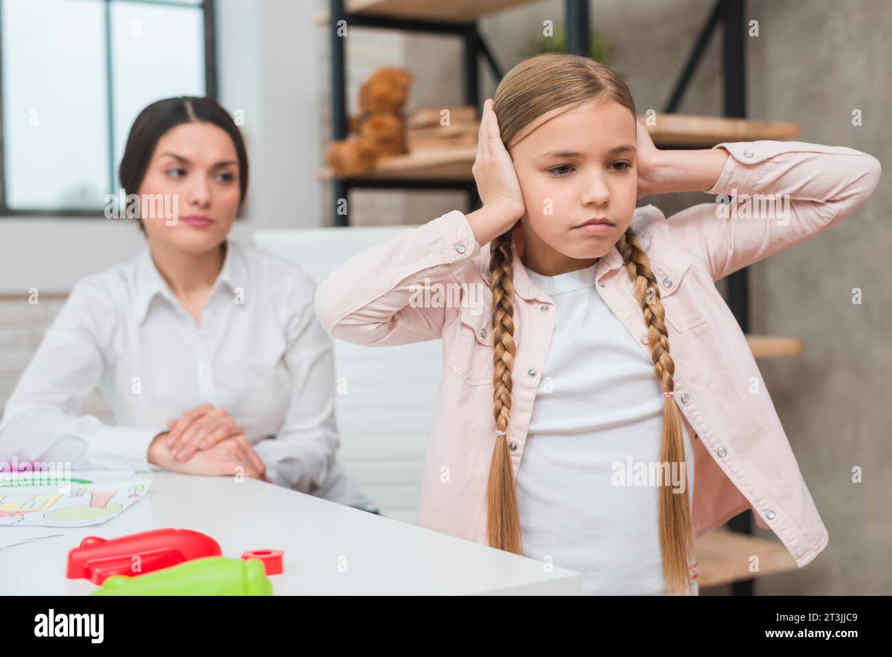 Close up female psychologist looking annoyed girl covering her ears with two hands Stock Photo