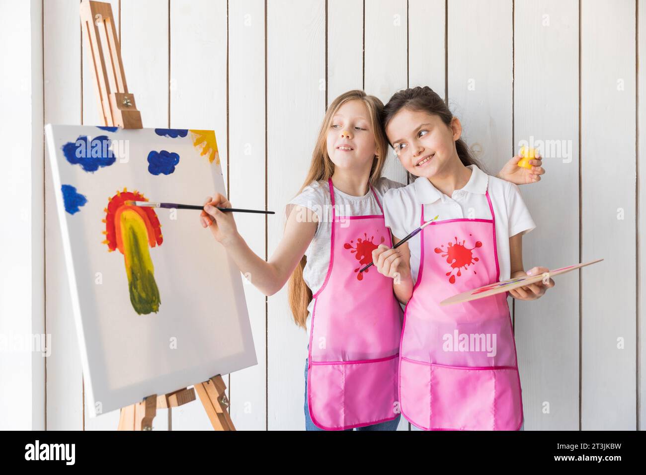 Happy girl holding palette hand looking her friend painting canvas with brush Stock Photo