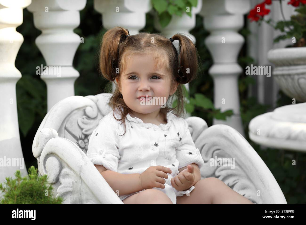 Cute little girl in white dress sitting in chair outdoors Stock Photo ...