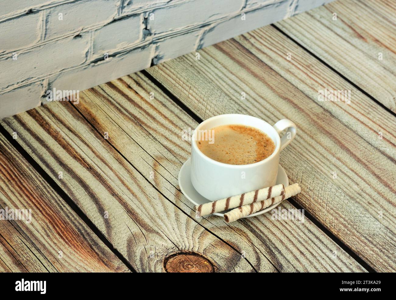 Fresh cappuccino with foam on a saucer with two wafer rolls on a light wooden table. Close-up. Stock Photo