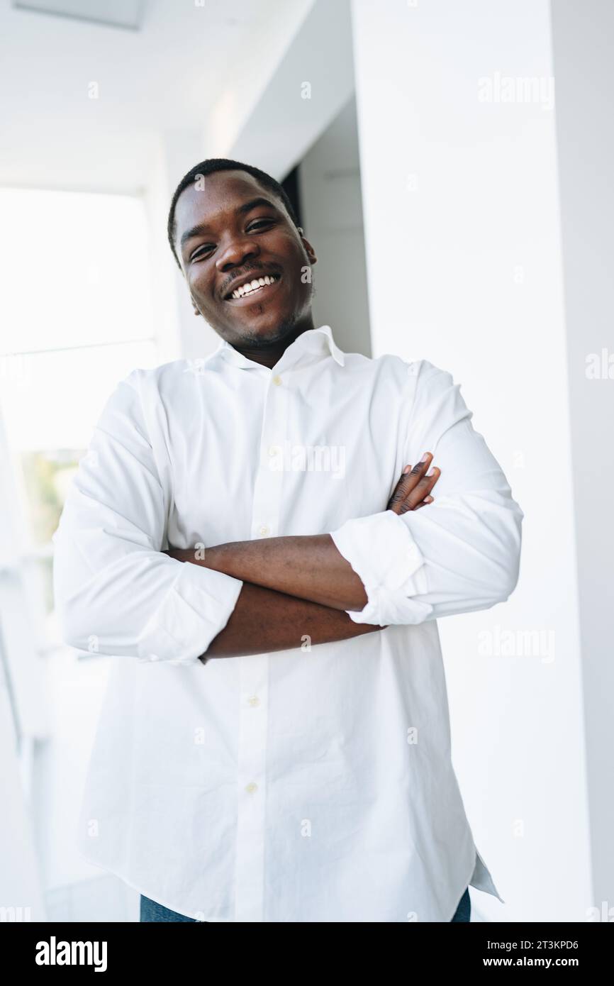Young african man in white shirt and glasses posing near large window ...