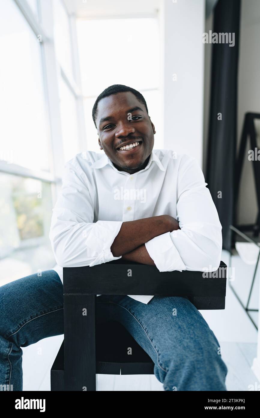 Young african man in white shirt and glasses posing near large window ...
