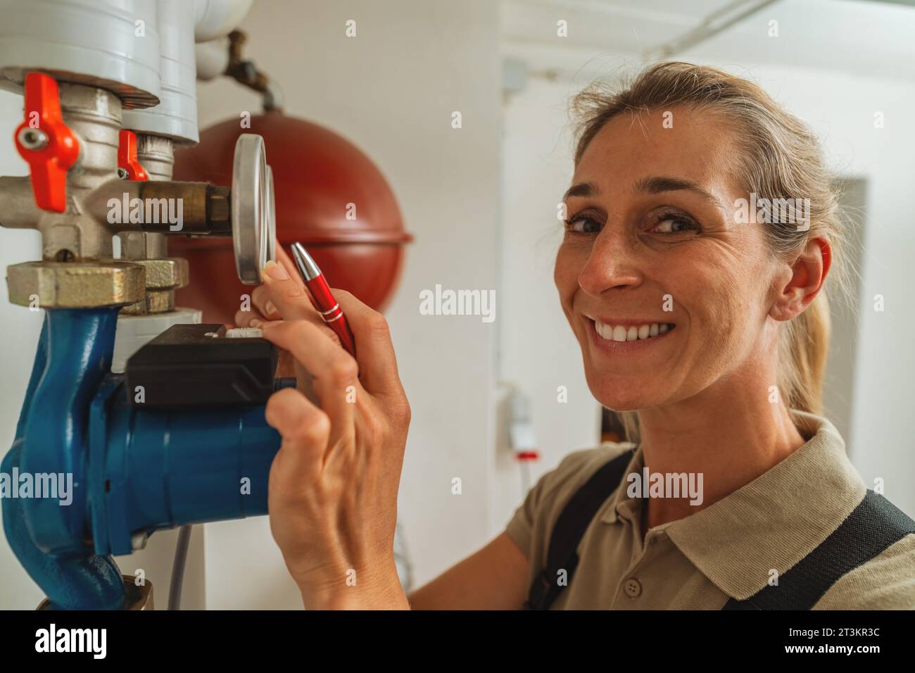 Happy female heating engineer checks gas thermostat at a boiler room with a old gas heating system. Gas heater replacement obligation concept image Stock Photo