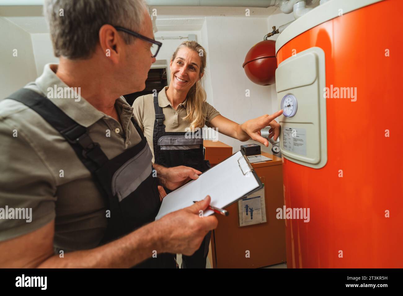 Team of heating engineers checks a old gas heating system thermostat, holding a Clipboard with checklist at a boiler room in a house. Gas heater repla Stock Photo