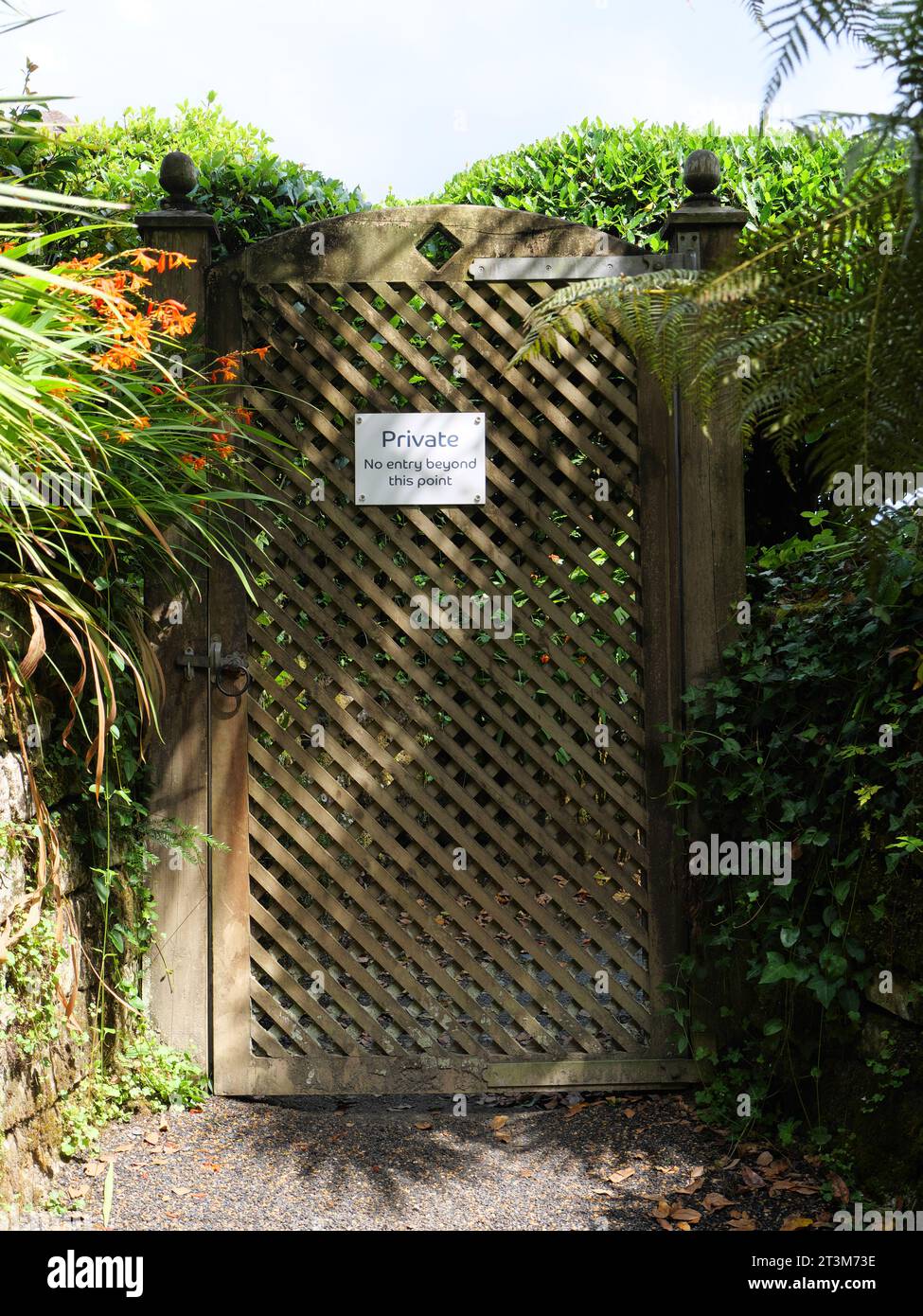 A latticed wooden garden gate with the inscription Private No entry beyond this point in the shade of the trees in Trebah Garden, Cornwall, England Stock Photo