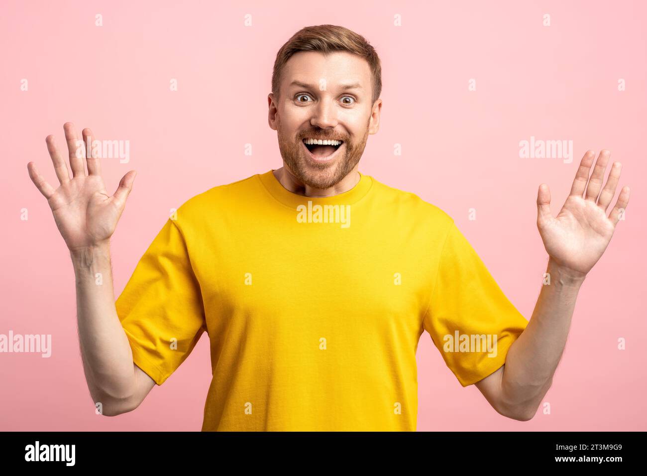 Amazed glad fun filled middle-aged bearded man with hands up looking at camera on pink background Stock Photo