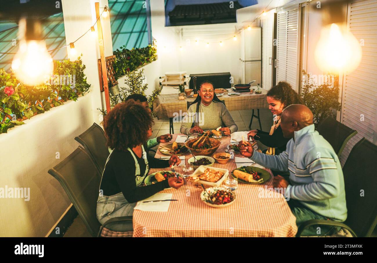 Happy african american family eating dinner together at home terrace outdoor - Holidays lifestyle concept - Soft focus on mother face Stock Photo