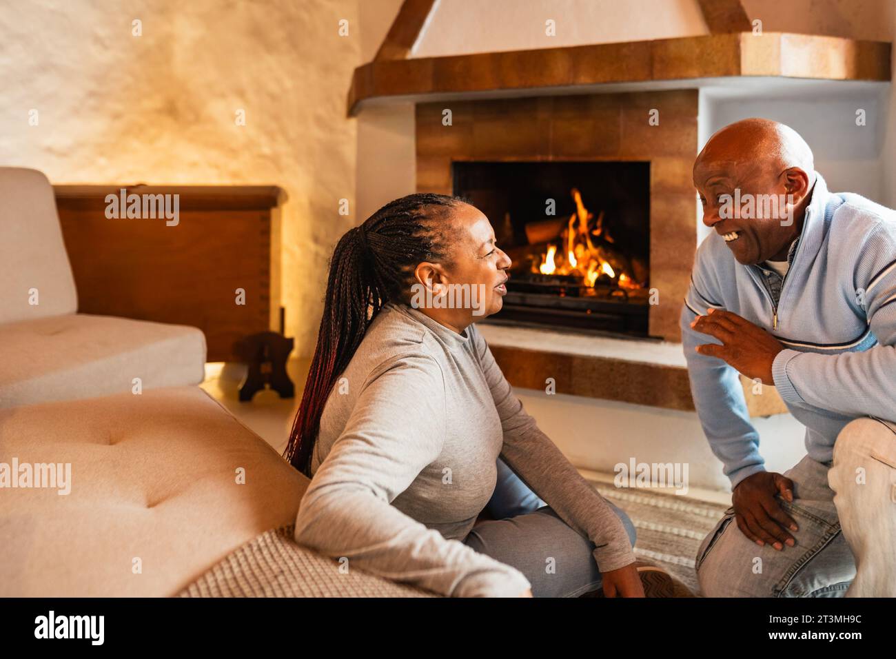 Happy African senior couple standing together close to fireplace in their rustic house Stock Photo