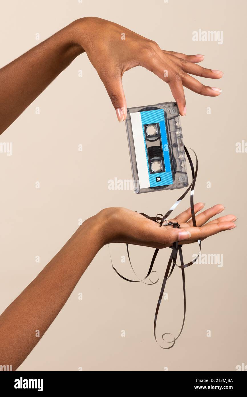 Side view of anonymous young ethnic female while standing in room and demonstrating vintage cassette with spilled out tape in manicured finger hands a Stock Photo