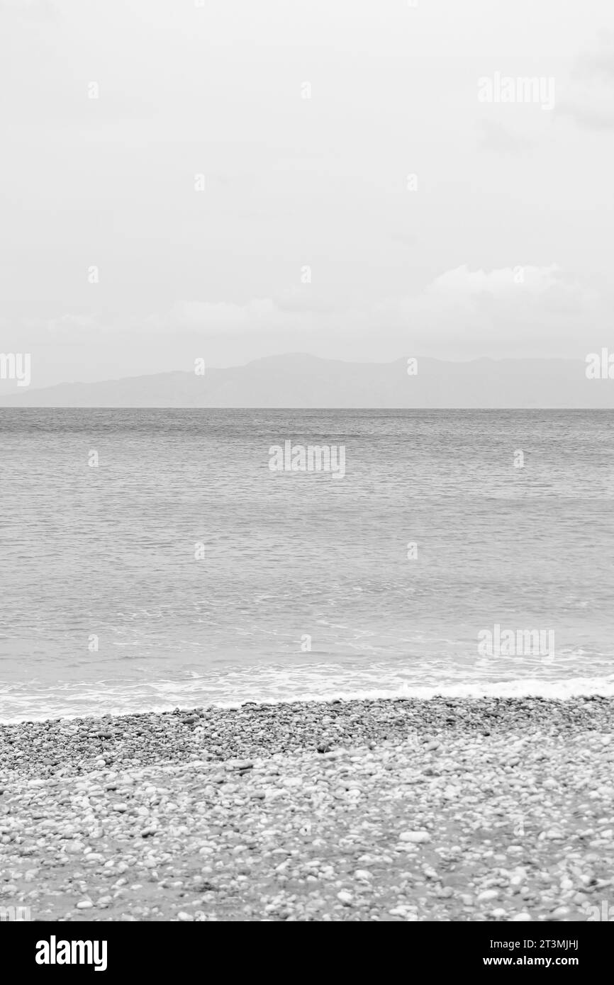 Clear water washing up on the shore at Paralia Ixia beach off Rhodes city in black and white Stock Photo