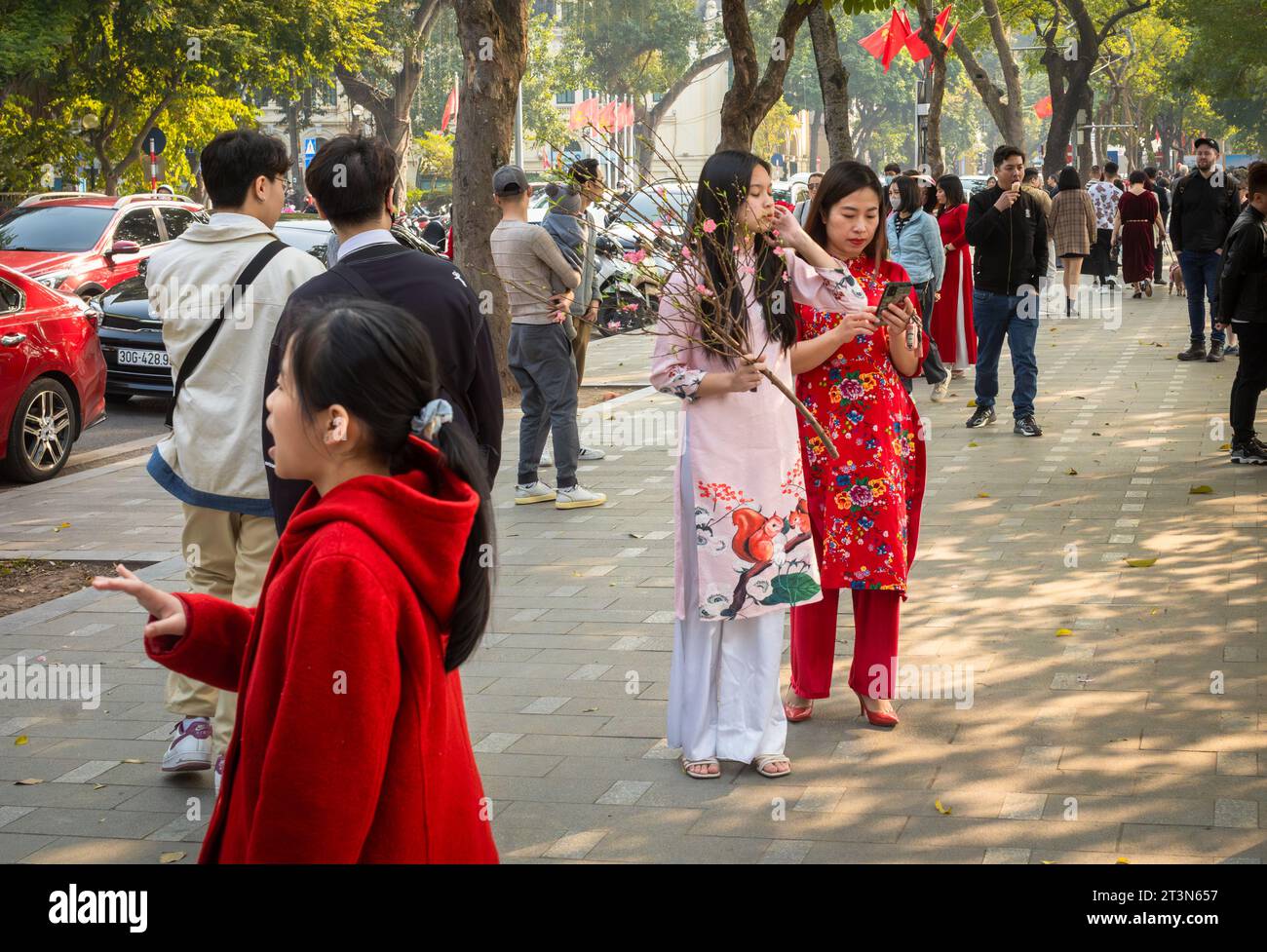 A Vietnamese mother with her daughter holding a peach blossom and both dressed in traditional ao dai at Tet, or lunar new year, in central Hanoi, Viet Stock Photo