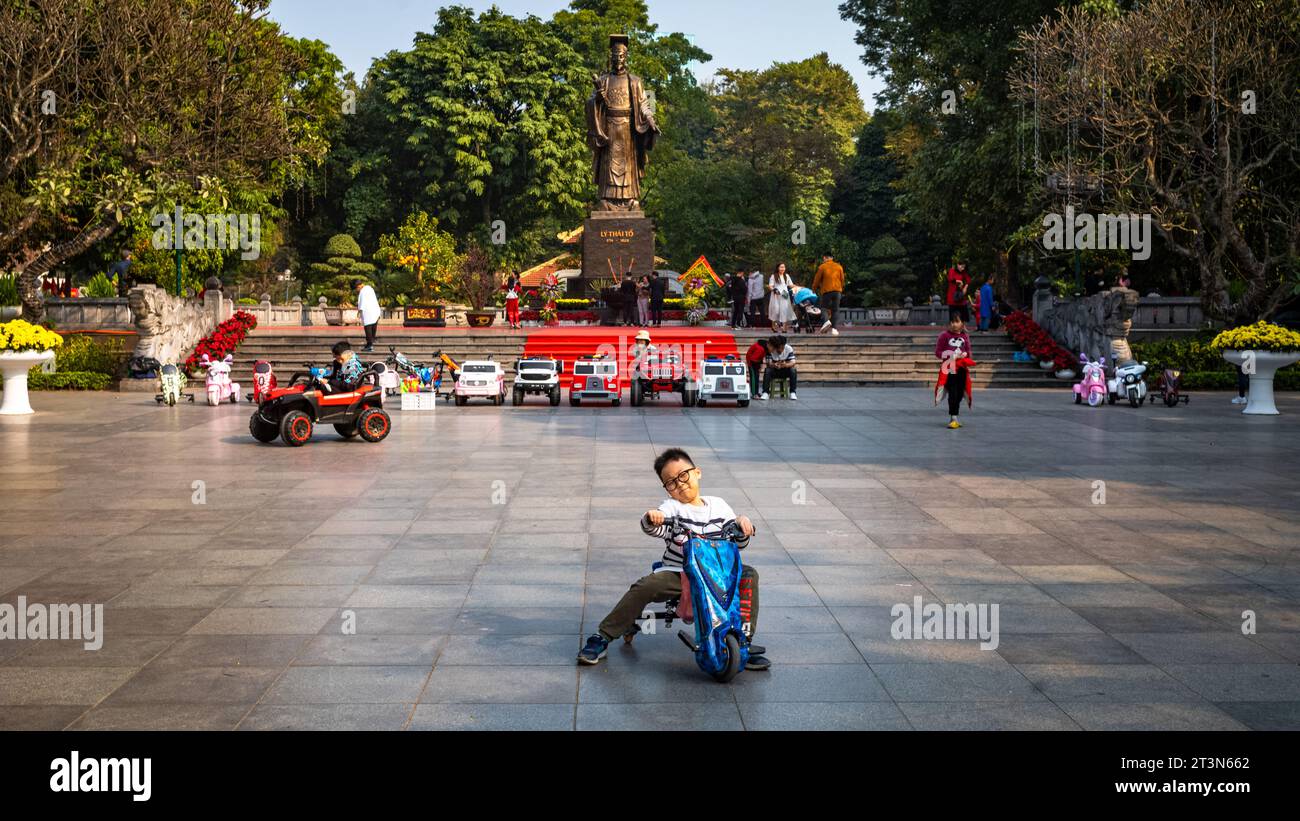 A young Vietnamese boy plays on a tricycle in front of the giant bronze statue of legendary emperor Ly Thai To in central Hanoi Stock Photo