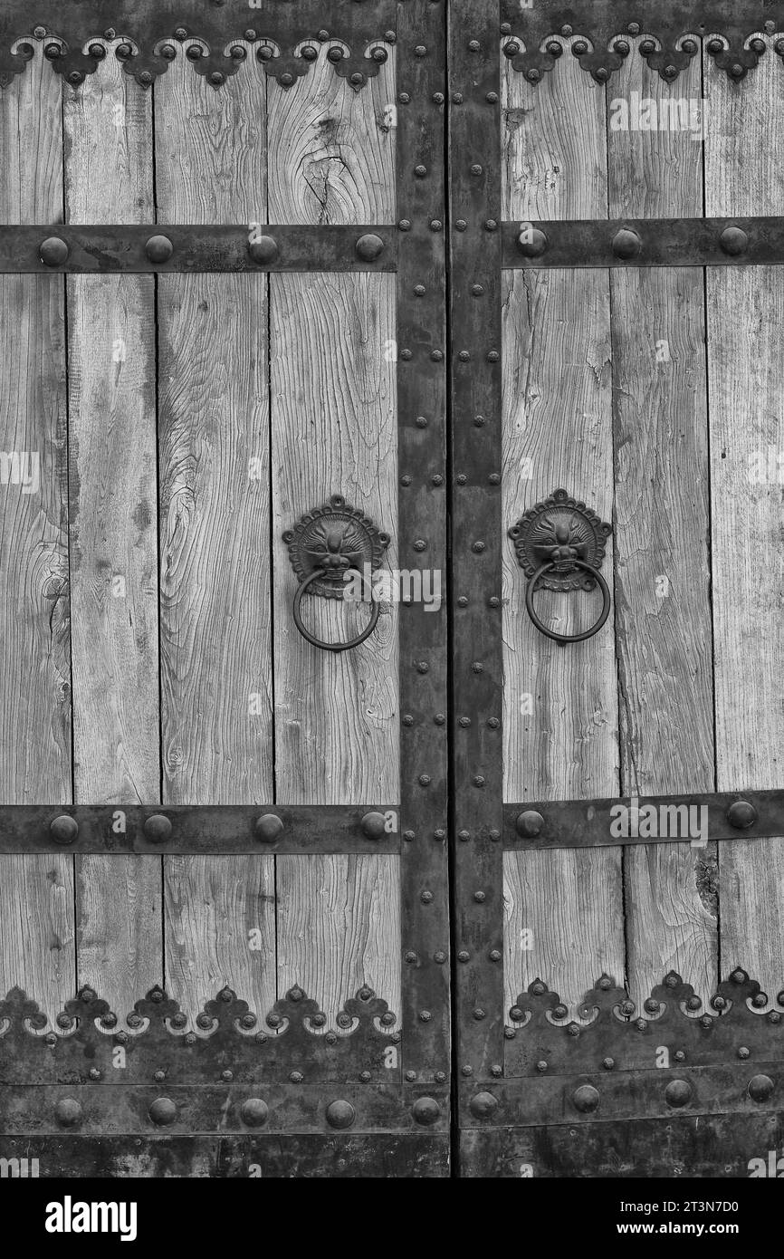 Black And White Photo Of A Simple Wooden Gate With Ornate Surrounding Metal Work In The 798 Art Zone, Dashanzi Art District, Beijing, China. Stock Photo