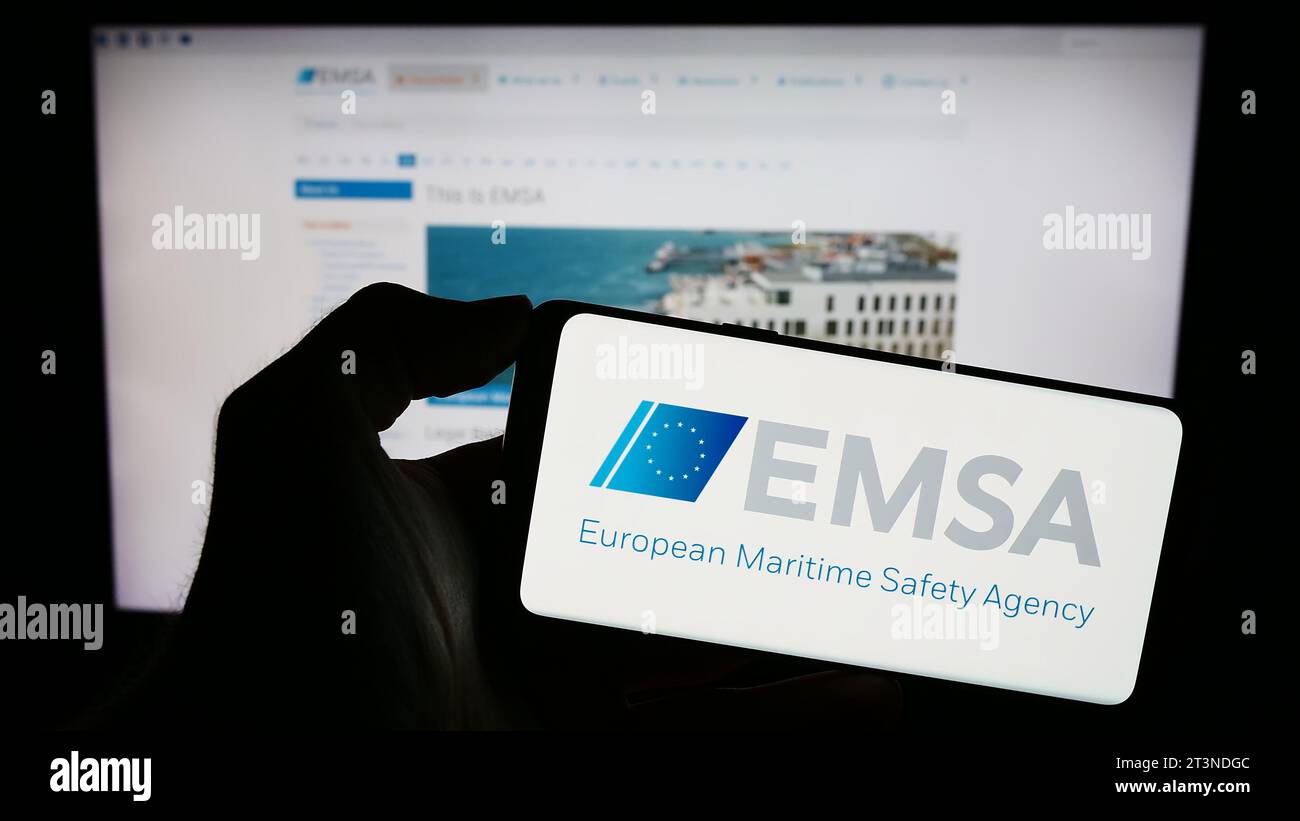 Person holding mobile phone with logo of EU institution European Maritime Safety Agency (EMSA) in front of web page. Focus on phone display. Stock Photo