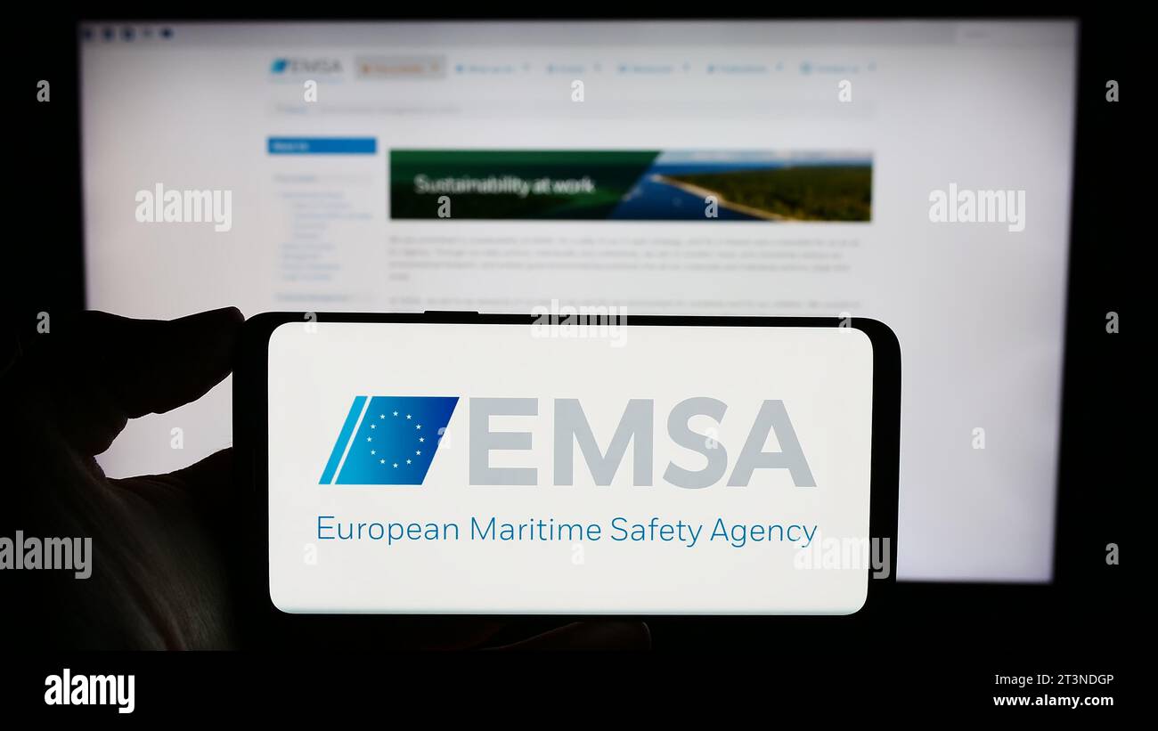 Person holding cellphone with logo of EU institution European Maritime Safety Agency (EMSA) in front of webpage. Focus on phone display. Stock Photo