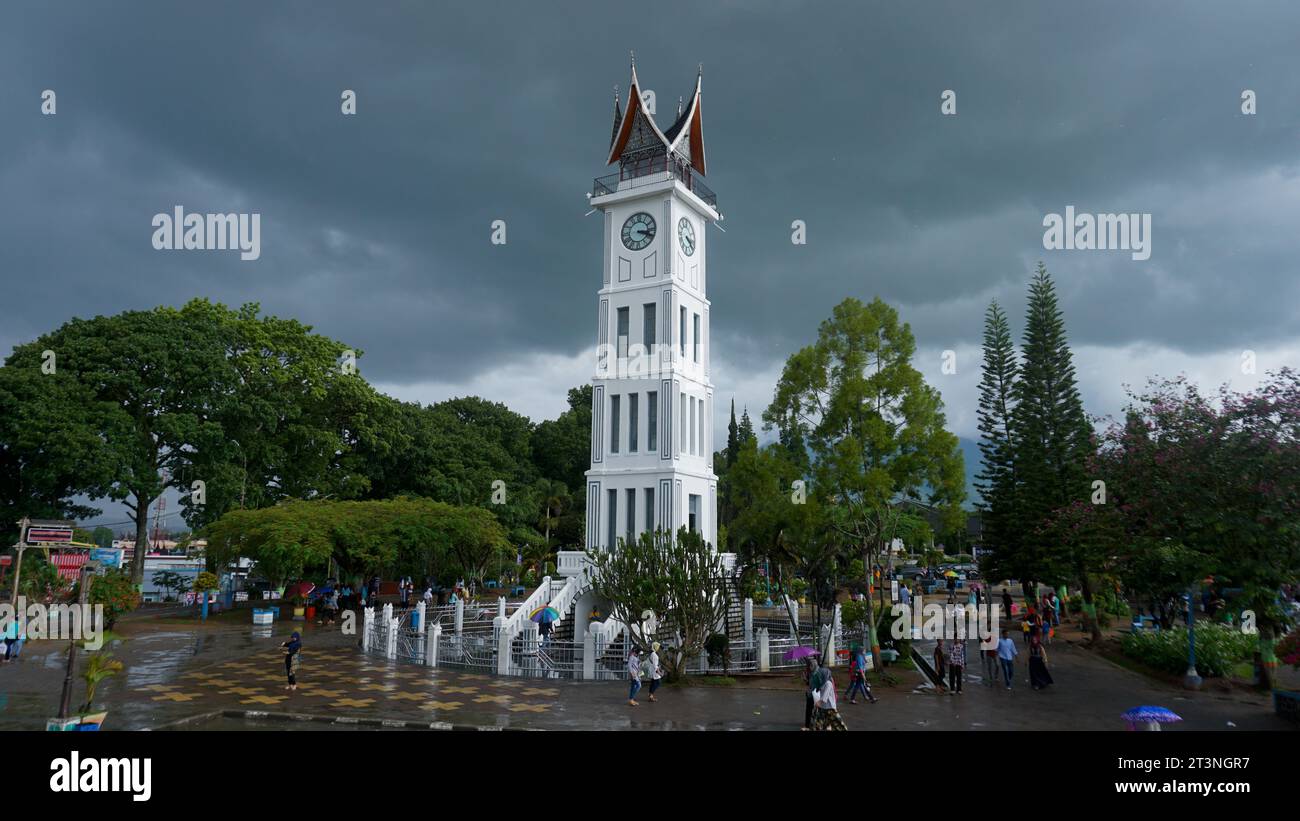 A view of the city of Bukitttinggi with its famous landmark Jam Gadang, bustling crowds, and lush greenery with a cloudy sky after the rain Stock Photo
