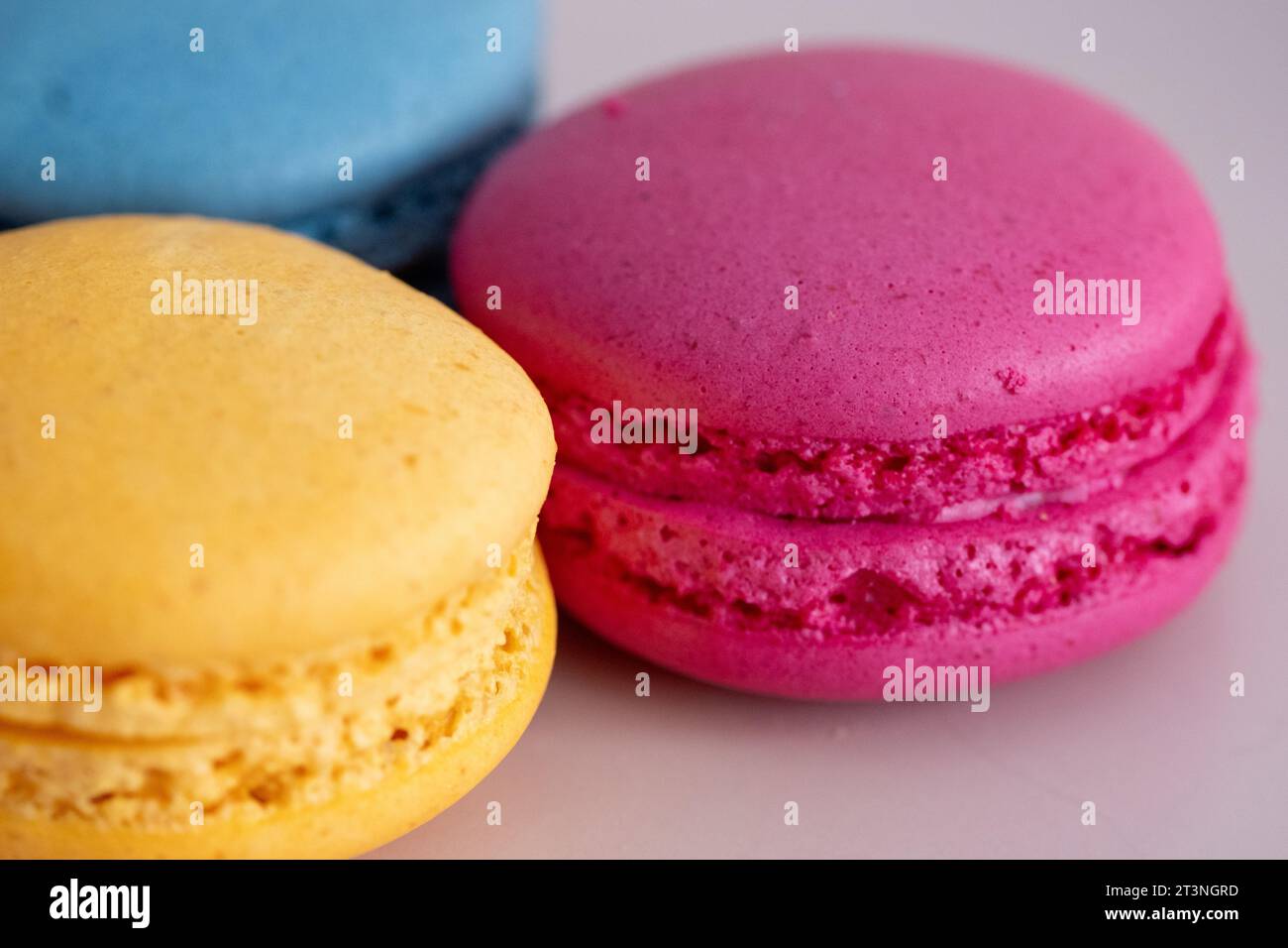 three different colored macarons on a pink plate on a blue background Stock Photo
