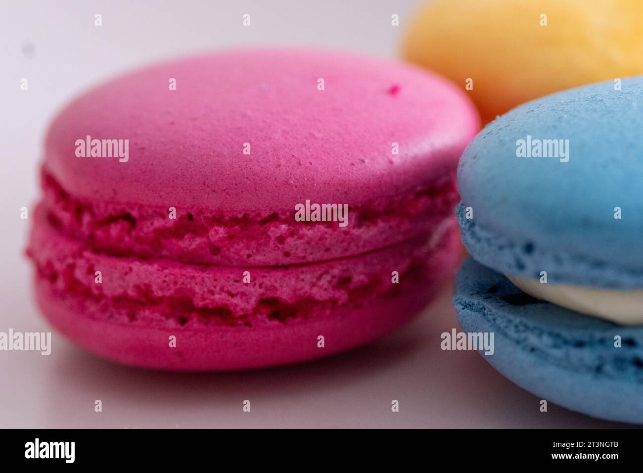 three different colored macarons on a pink plate on a blue background Stock Photo