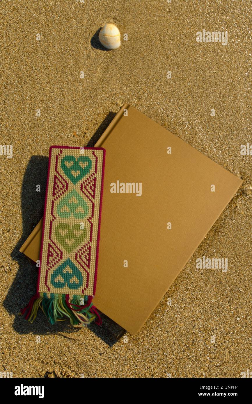 Hardback book with decorated bookmark on a sandy beach, with a nearby shellfish Stock Photo