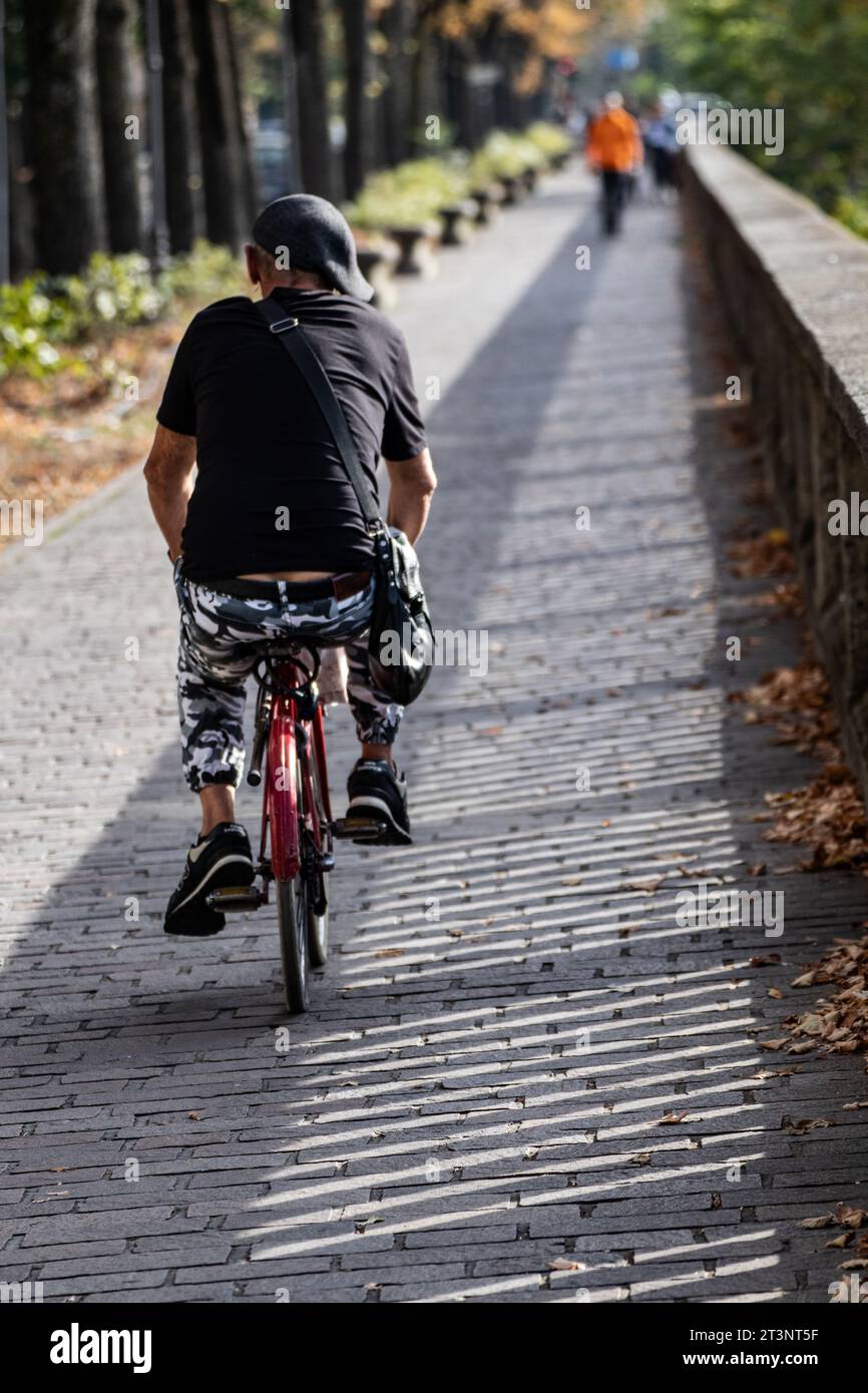 elderly man cycling on city sidewalk Stock Photo