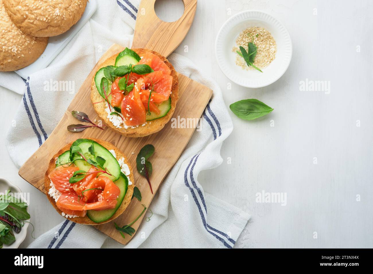 Open smoked salmon sandwiches with cream cheese, cucumber, sesame seeds, microgreens, spinach, and peas leaves on light old wooden background. Healthy Stock Photo