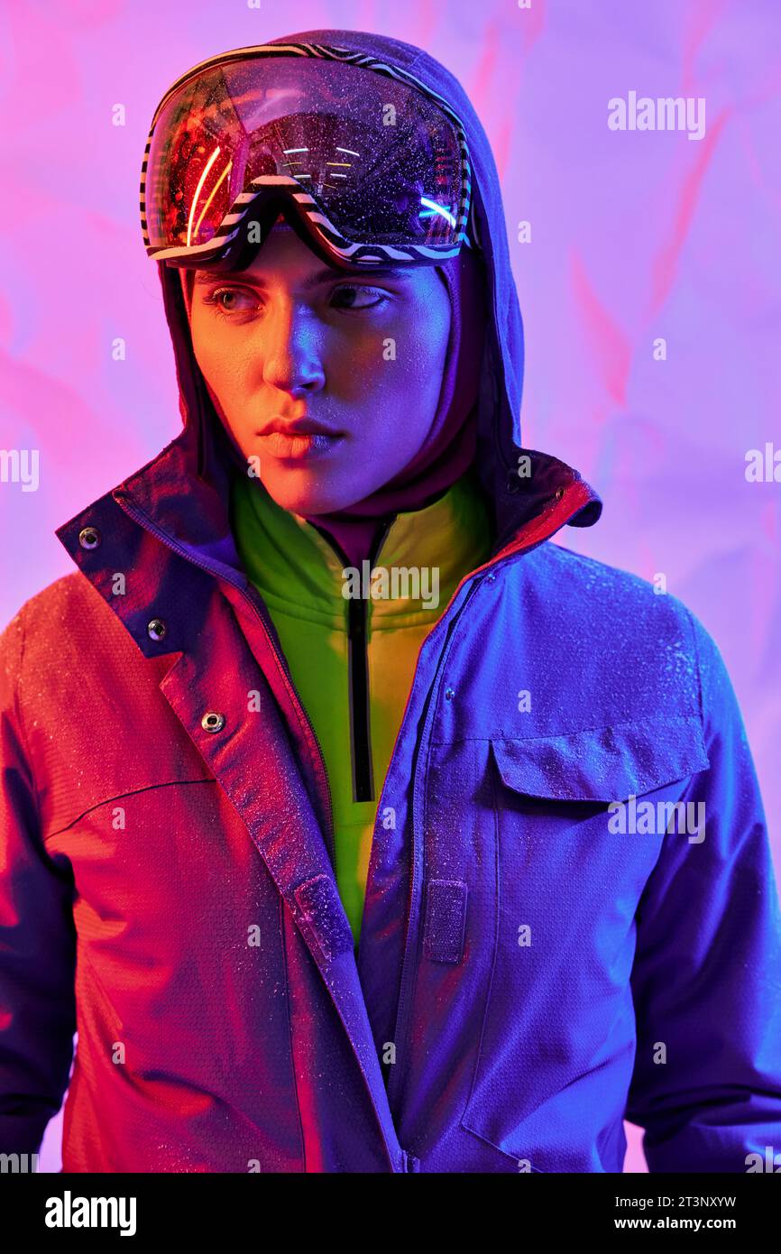 beautiful woman in ski mask and googles wearing warm jacket on purple