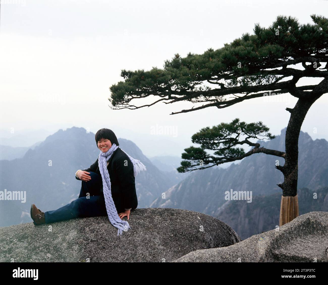 China. Anhui. Huangshan mountains. Chinese young woman sitting on rock. Stock Photo