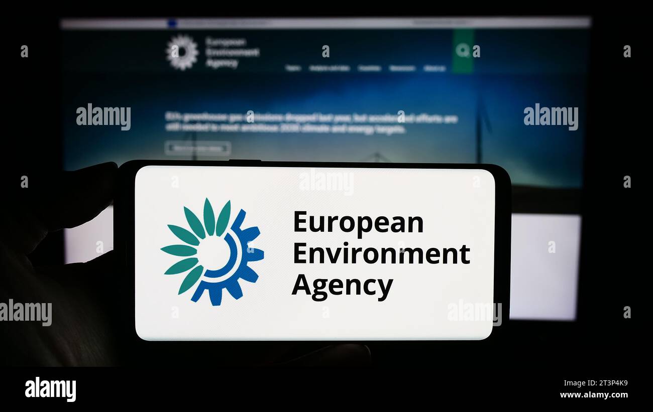 Person holding cellphone with logo of EU institution European Environment Agency (EEA) in front of webpage. Focus on phone display. Stock Photo