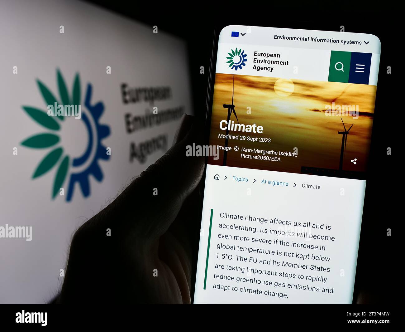 Person holding cellphone with webpage of EU institution European Environment Agency (EEA) in front of logo. Focus on center of phone display. Stock Photo