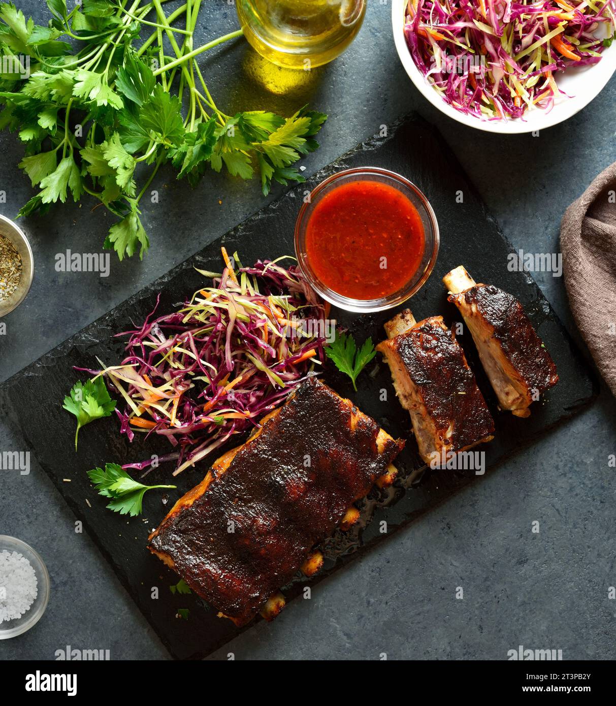 Spicy grilled spare ribs with red cabbage salad and sauce on board over dark stone background. Top view, flat lay Stock Photo